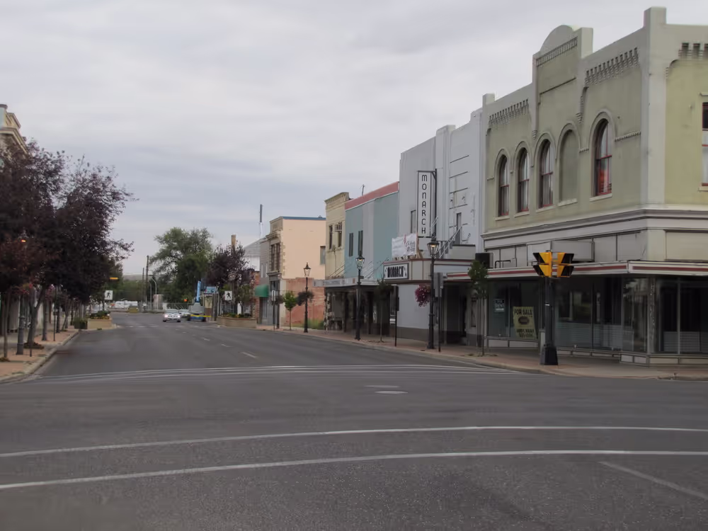 A quiet, empty street in a small town with a mix of older buildings and shops on both sides.